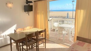 Ein Zimmer mit Esstisch, Stühlen, einem Bett, einem Fernseher und einem Balkon mit Blick auf den Strand.