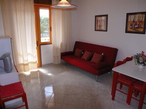 Ein Wohnzimmer mit einem roten Sofa, einem weißen Tisch und Stühlen, einem Fernseher und zwei gerahmten Bildern an der Wand.