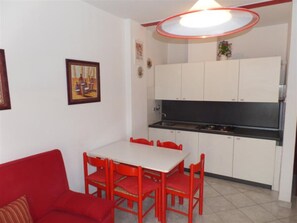Una cucina compatta con mobili bianchi, un piano cottura nero e una zona pranzo con tavolo e sedie rossi.