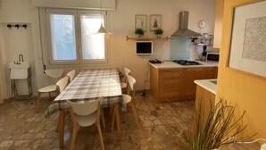 Een kleine keuken met een eettafel, stoelen, een fornuis en een kleine televisie.