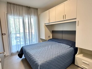 Een slaapkamer met een bed, een raam met gordijnen, een deur en een kledingkast.