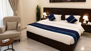 A hotel room with a large bed, a chair, a nightstand, a lamp, and a painting of a sunset over the ocean.