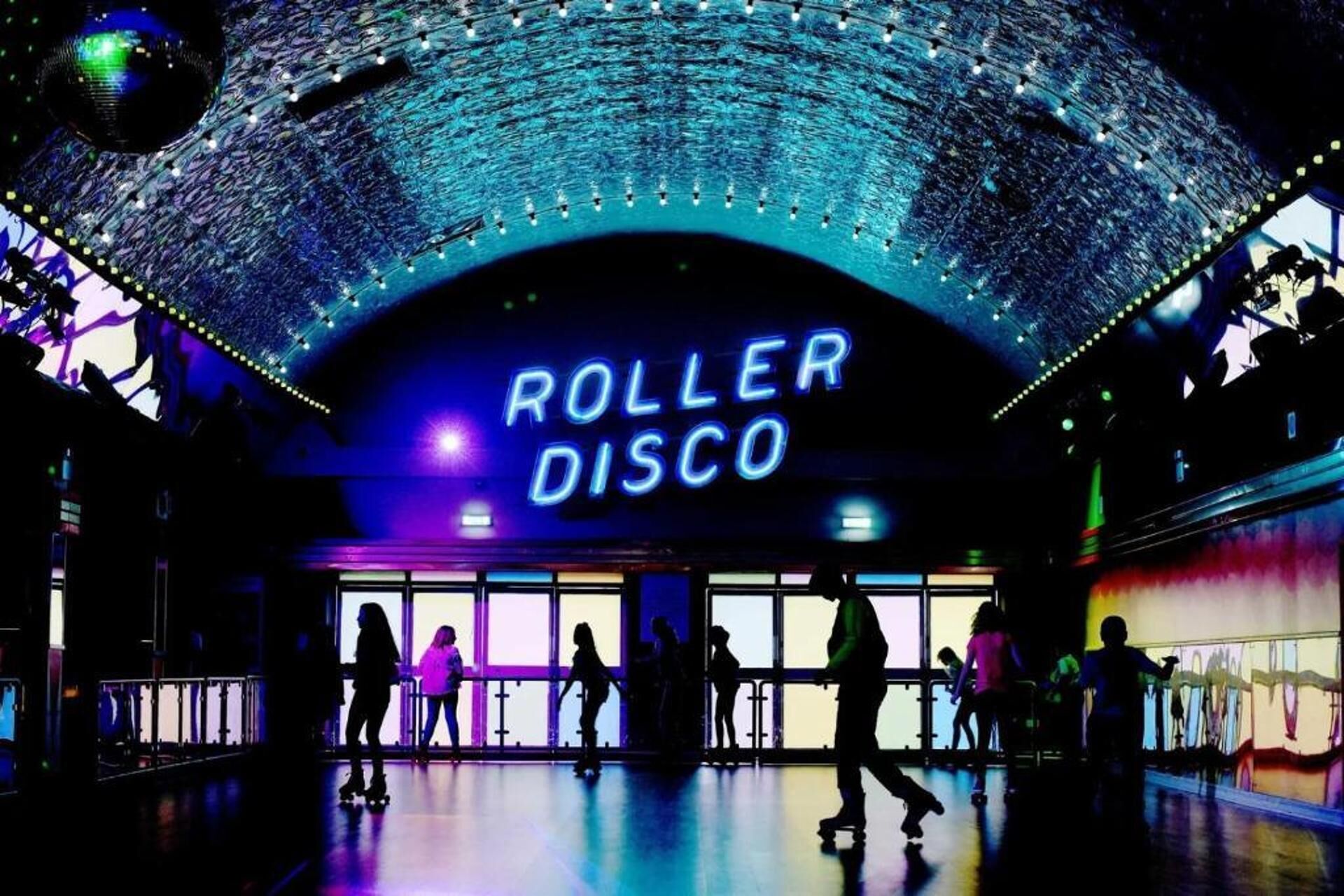 Une discothèque sur patins avec une enseigne au néon, des gens qui patinent et un plafond incurvé illuminé.