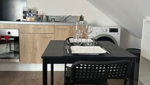 Eine kompakte Küche mit Essbereich, darunter ein Tisch für zwei Personen gedeckt mit Gläsern und Besteck, eine Waschmaschine und eine Mikrowelle.
