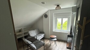 Ein Loft-Zimmer mit hohen Decken, einem Bett, einem kleinen Tisch und einem Fenster mit Blick auf Grünflächen.