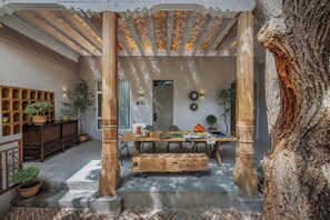 Una mesa de madera con sillas, un banco y una pared con estantes y plantas en macetas.