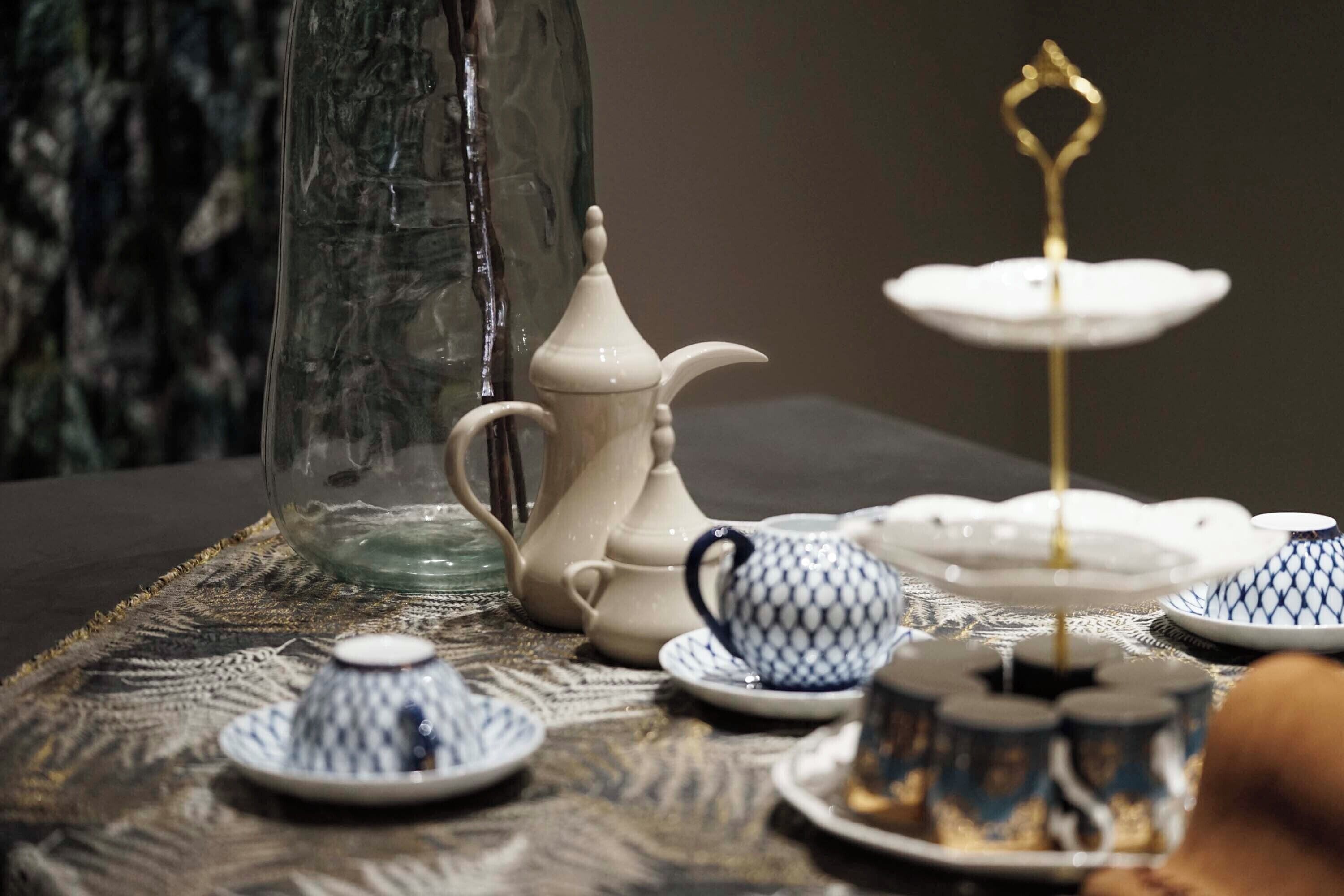 A table with a glass pitcher, teapot, teacups, and a tiered stand.