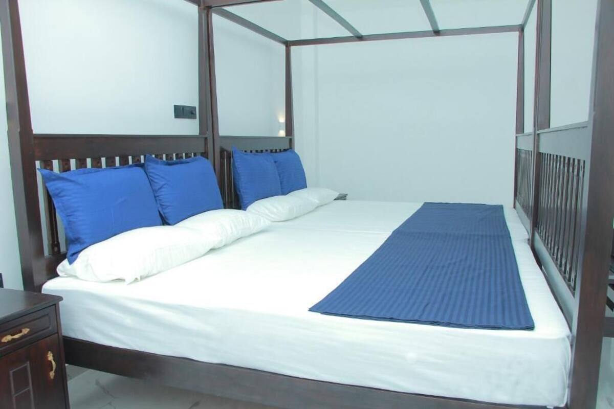 Una cama con dosel con ropa de cama blanca y azul, una mesita de noche de madera y un pasamanos de metal.