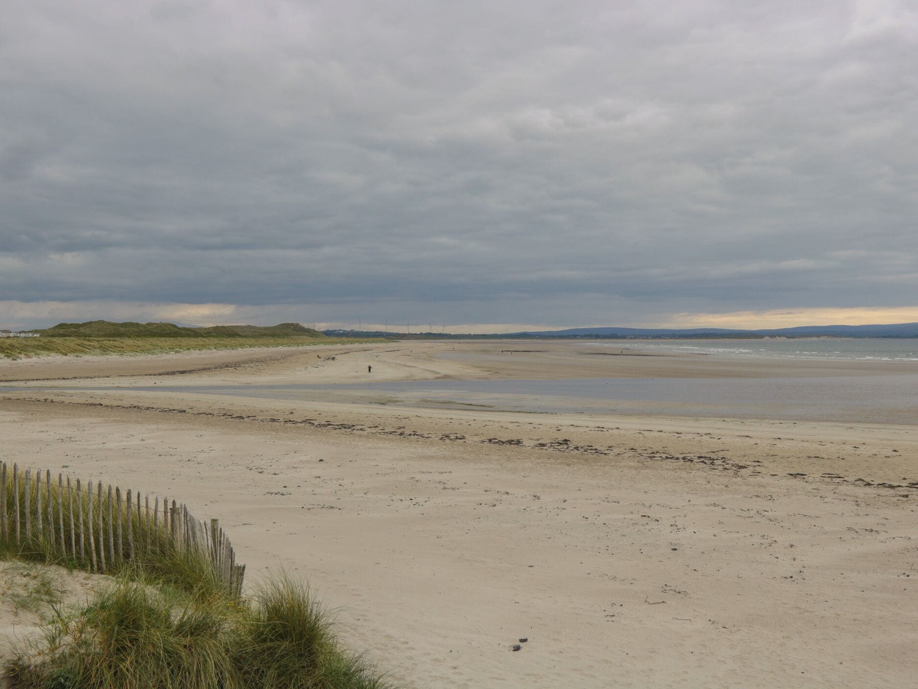 A beach with dunes and a fence.