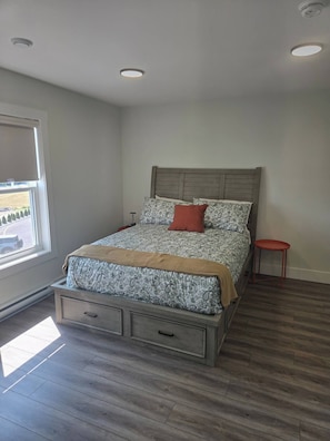 A bedroom with a bed, a window, a small table, and a ceiling light.