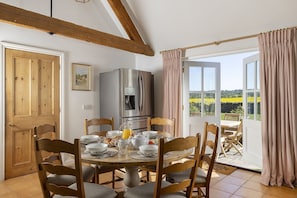 Comedor con una mesa redonda, sillas, refrigerador y vista a un campo a través de una puerta de vidrio.