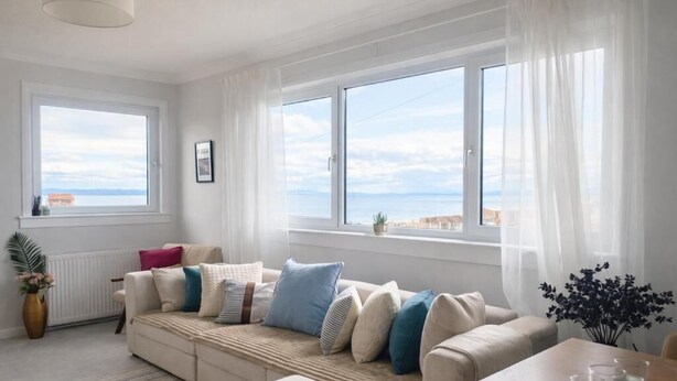 A living room with a sofa, a table with glasses, a plant, and a view of the sea. - The Station House Boutique Hotel (Burghead)
