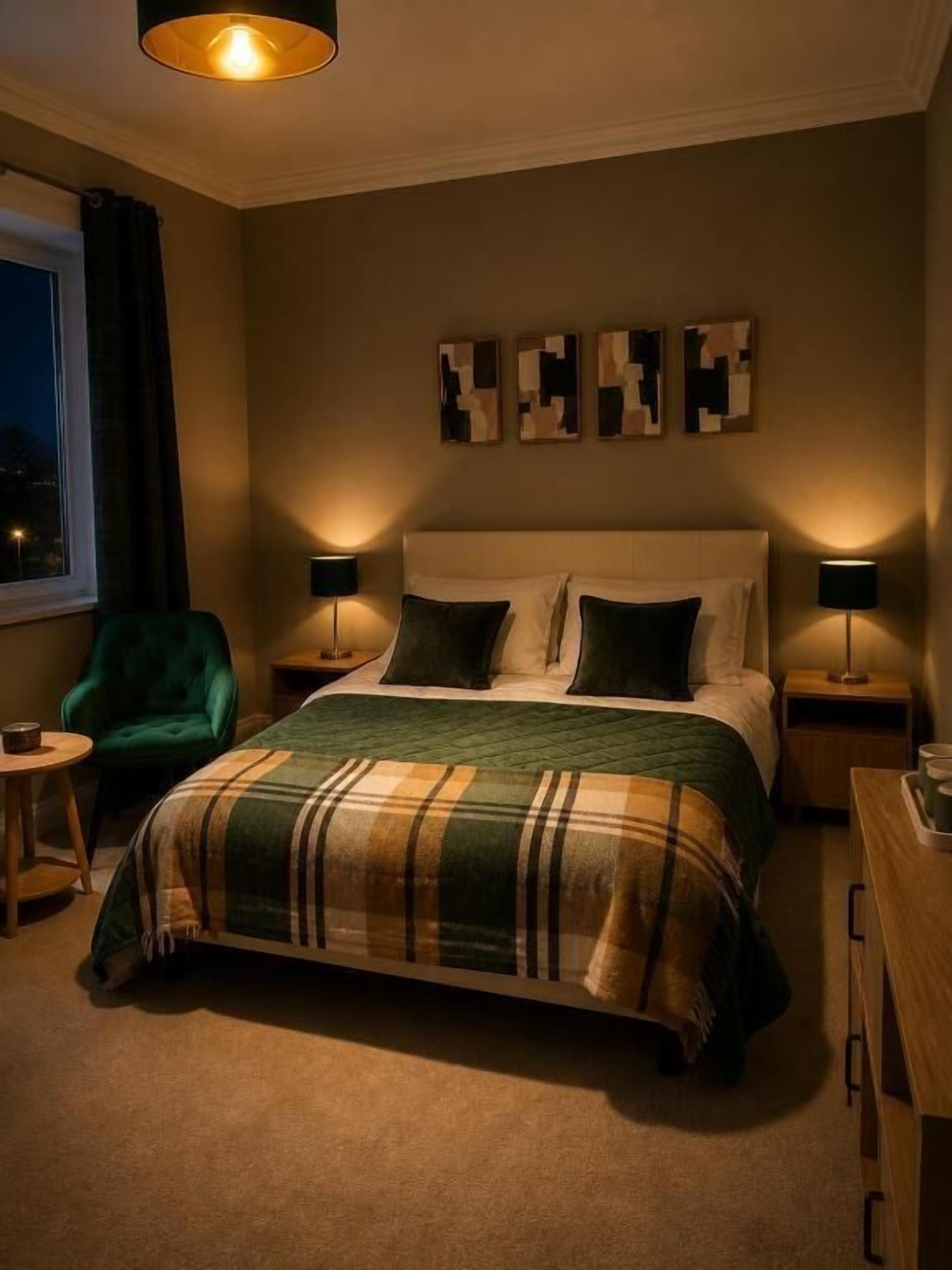 A bedroom with a bed, two bedside tables, a green chair, and artwork on the wall.