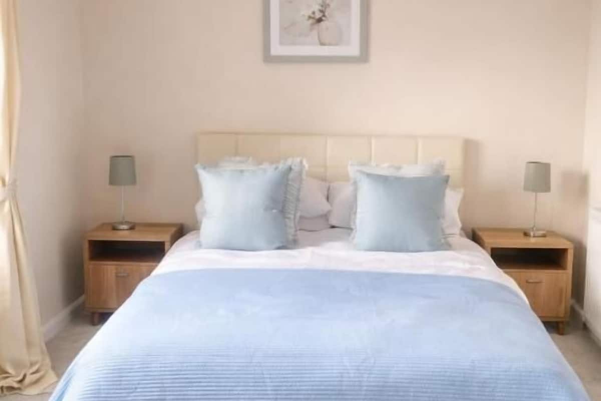 A bedroom with a bed, two bedside tables, a hanging light fixture, and a framed picture on the wall.