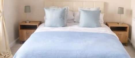Un dormitorio con cama, dos mesitas de noche, una lámpara colgante y un cuadro en la pared.