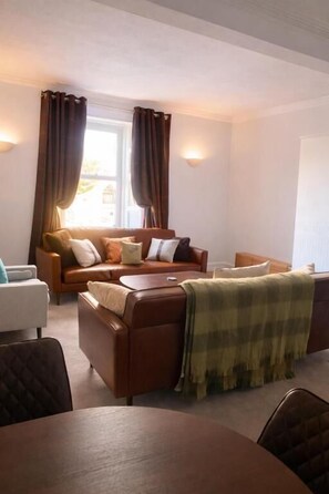 A living room with a sofa, a coffee table, and a dining table. - The Station House Boutique Hotel (Burghead)