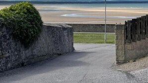 A paved pathway leading to a beach with a stone wall and a lamppost. - The Station House Boutique Hotel (Burghead)
