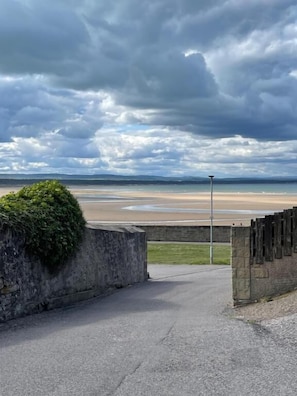 A paved pathway leading to a beach with a stone wall and a lamppost. - The Station House Boutique Hotel (Burghead)