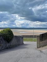 A paved pathway leading to a beach with a stone wall and a lamppost.