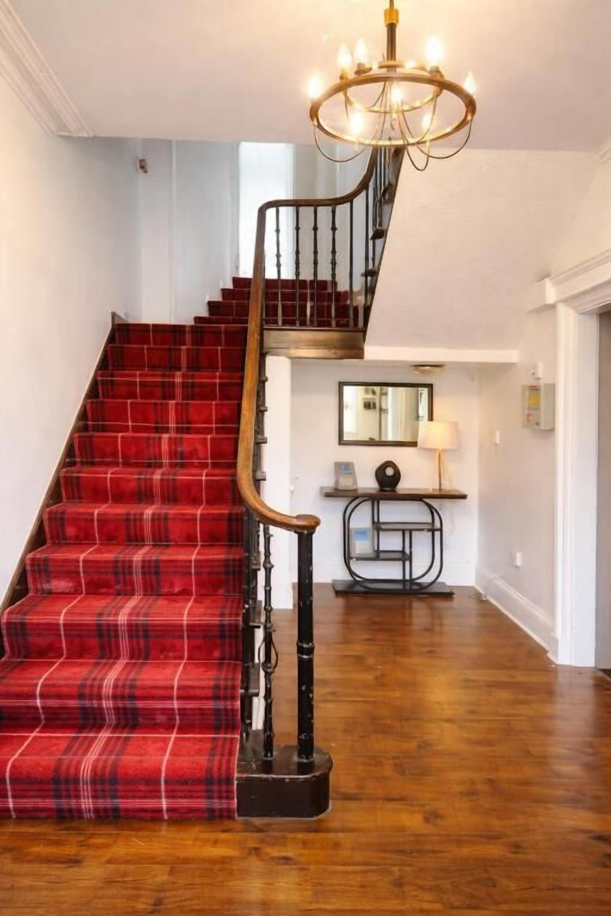 A staircase with a red plaid carpet, a black metal railing, and a chandelier.