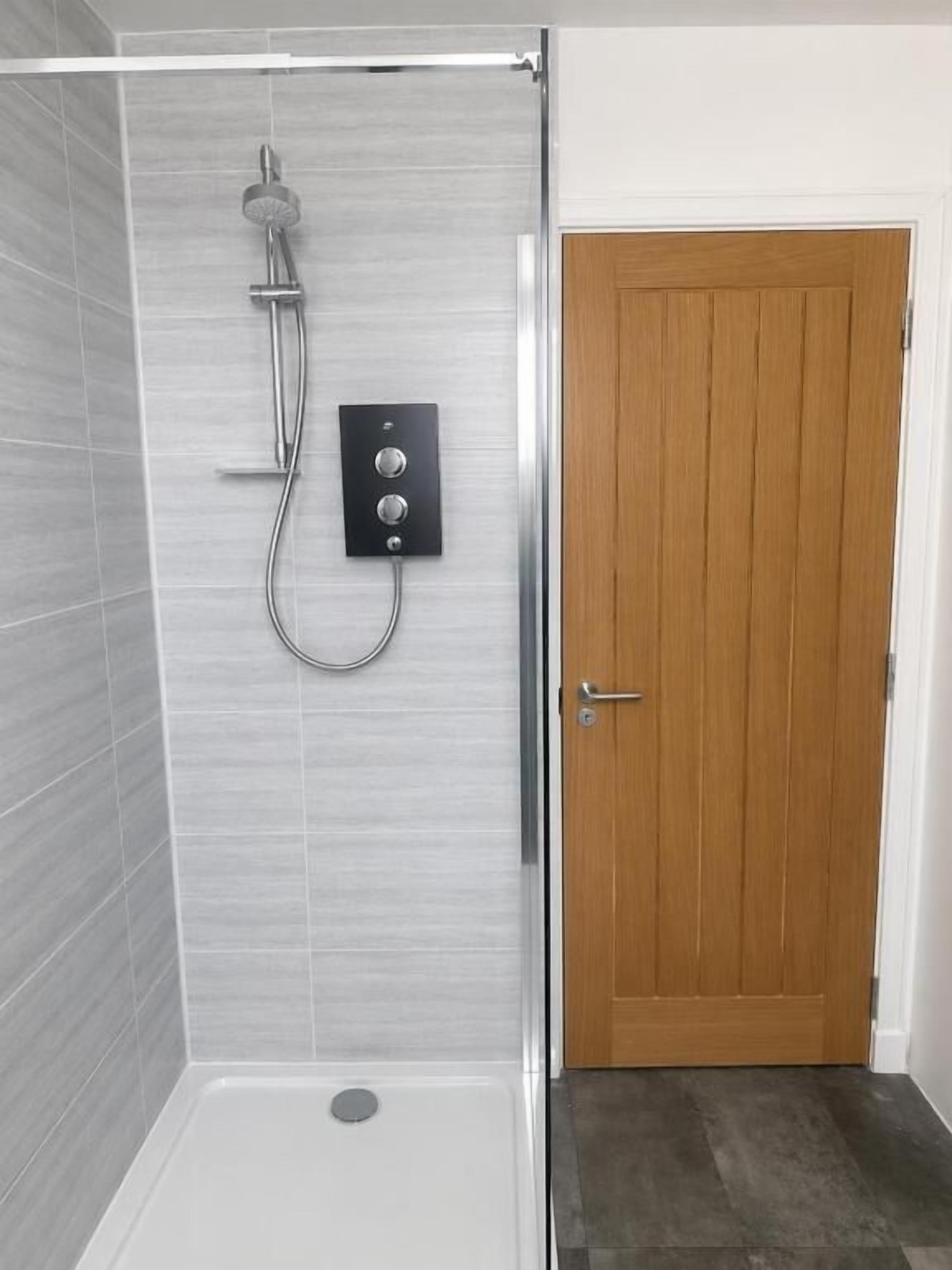 Une douche équipée d’un pommeau de douche à main, d’un panneau de commande et d’une porte avec une poignée.