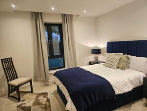 Ein Schlafzimmer mit einem Bett, einem Sessel, einem Nachttisch und einem Fenster mit Vorhängen.