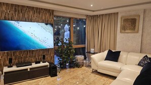 A living room with a large flat-screen TV, a white leather sofa, a small side table, and a potted plant. - Minutes from tube, exclusive central london location. Huge garden and spacious (London)