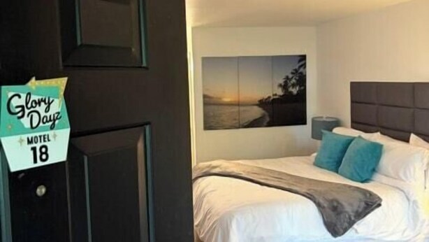 A hotel room with a bed, a nightstand, a wall-mounted picture, and a door with a sign. - King Suite #18 at Glory Dayz (Eureka Springs)