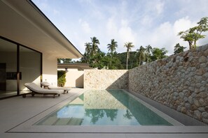 Ein moderner Poolbereich im Freien mit Liegestühlen, einer Steinmauer und Blick auf Palmen.