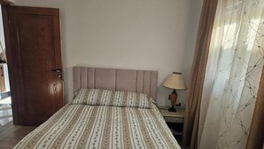 Ein Schlafzimmer mit Bett, Nachttisch, Lampe, Tür und Vorhang.