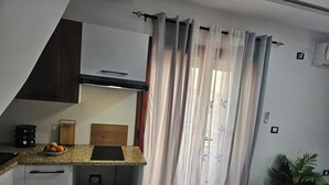 Eine Küche mit einer Granit-Arbeitsplatte, einer schwarzen Induktionskochplatte, einem Holzschneidebrett und einer Fruchtschüssel.