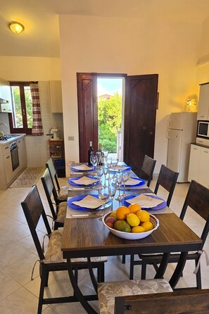 A dining area with a table set for six, a bowl of fruit, and a view of the outdoors. - Two double rooms with a beautiful ocean view in Costa Rei   (Costa Rei)