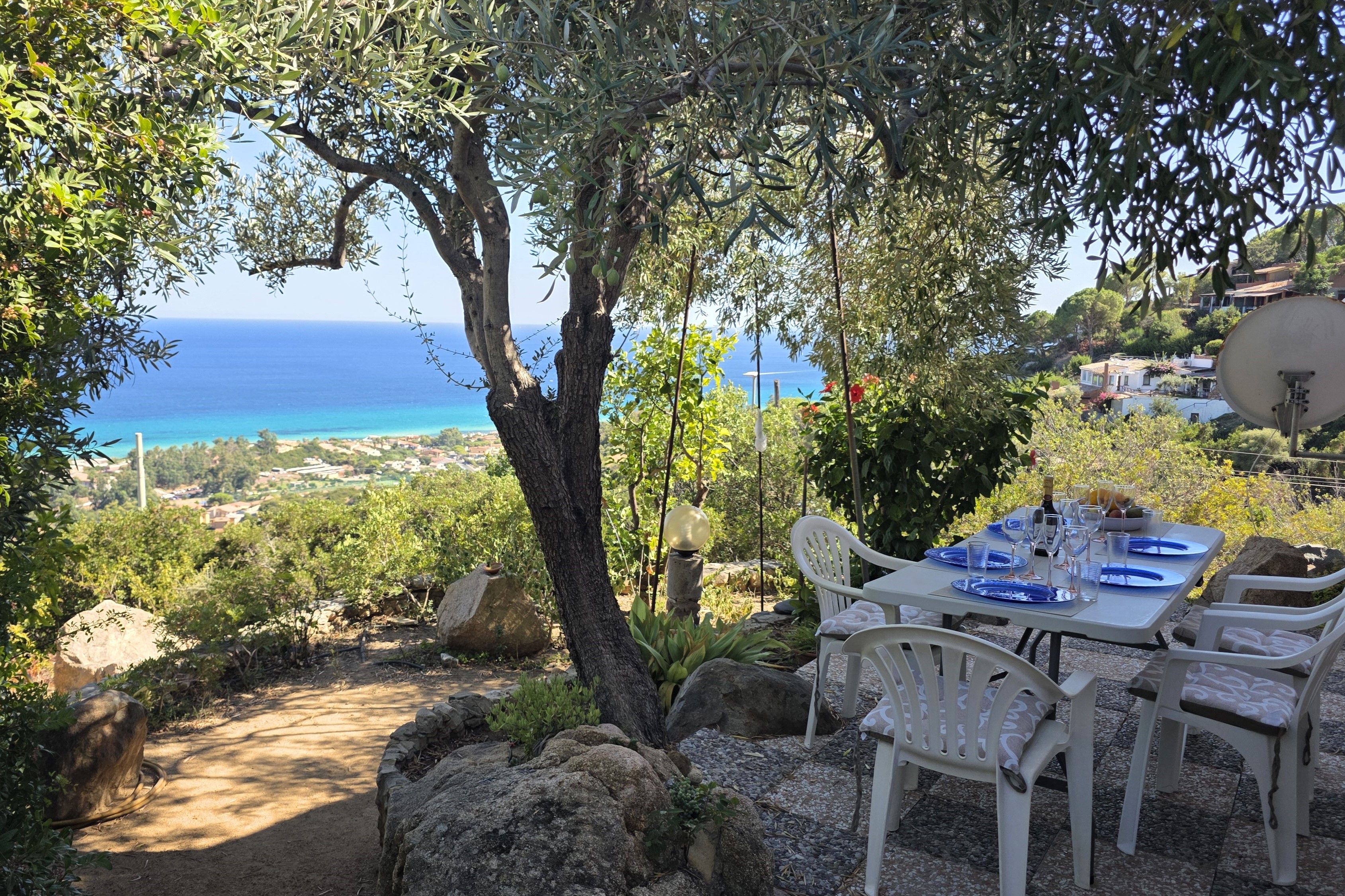 Un espace de restauration en plein air avec une table dressée pour deux personnes, offrant une vue sur un paysage côtier.