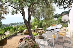 An outdoor dining area with a table set for two, surrounded by rocks and plants, overlooking a coastal view. - Two doubles with beautiful sea views in Costa Rei (Costa Rei)