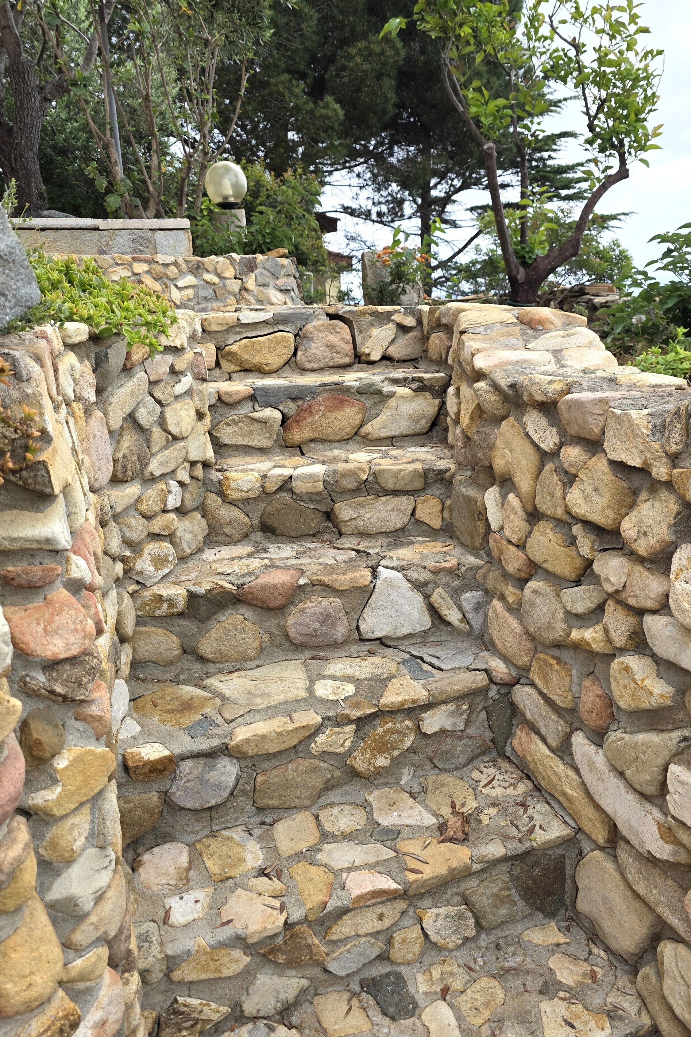 A stone staircase with a lantern on top, surrounded by greenery.