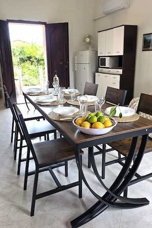 A dining area with a long table set for six, chairs, a bowl of fruit, and a kitchen in the background. - Two doubles with beautiful sea views in Costa Rei (Costa Rei)