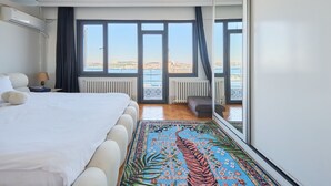 Een hotelkamer met een groot bed, uitzicht op zee, een radiator en een raam met gordijnen.