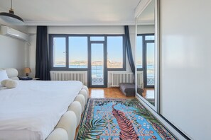 Ein Hotelzimmer mit einem großen Bett, Meerblick, Heizkörper und einem mit Vorhängen versehenen Fenster.