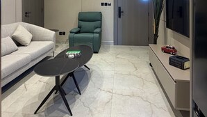 A modern living room with a sofa, a green chair, a coffee table, a flat-screen TV, and a marble floor. - 301 Tara-jre Jabal Al Lweibdeh With Stunning View (Amman)