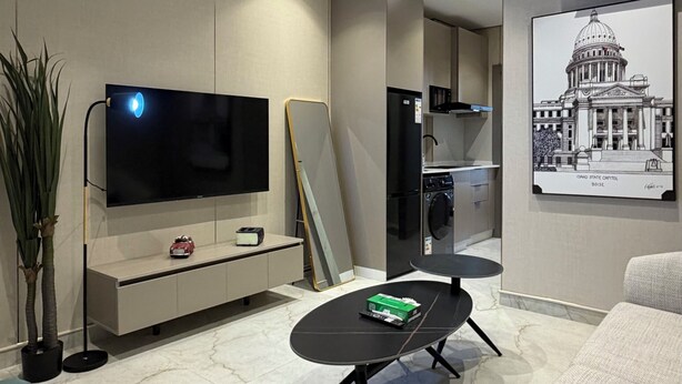 A modern living room with a flat-screen TV, a dining table, a sofa, and a kitchen area with a refrigerator and microwave. - 301 Tara-jre Jabal Al Lweibdeh With Stunning View (Amman)