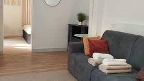 Ein modernes Wohnzimmer mit einem grauen Sofa, einem kleinen runden Tisch und einer Topfpflanze.