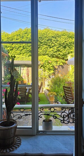 Blick durch eine Glastür auf eine Terrasse mit Kaktus, Stühlen und einem Garten.