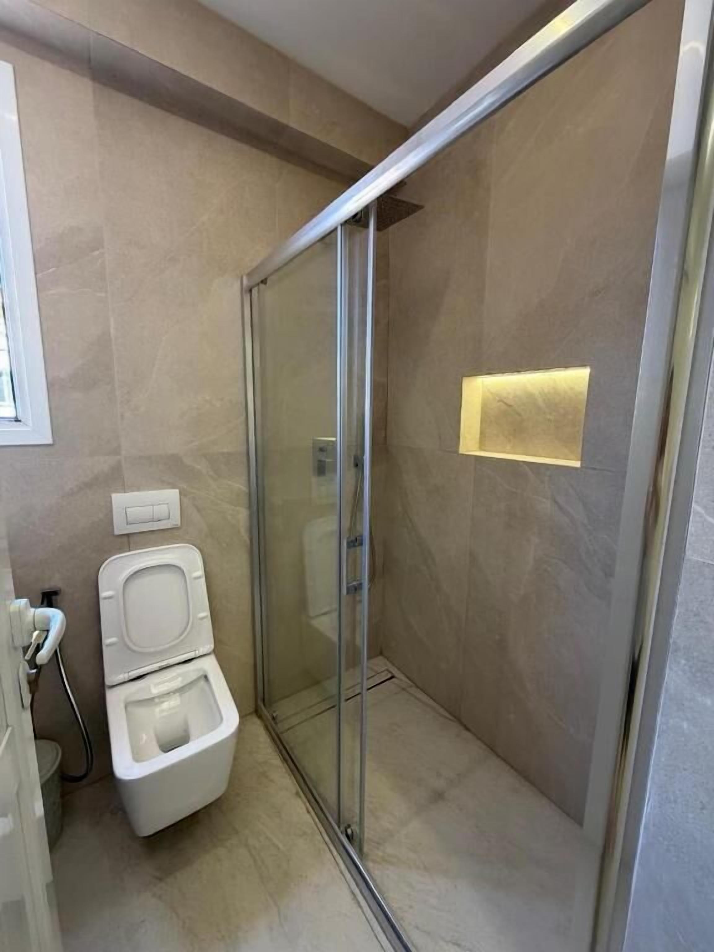 Casa de banho com cabine de duche em vidro, sanita e candeeiro fixo na parede.