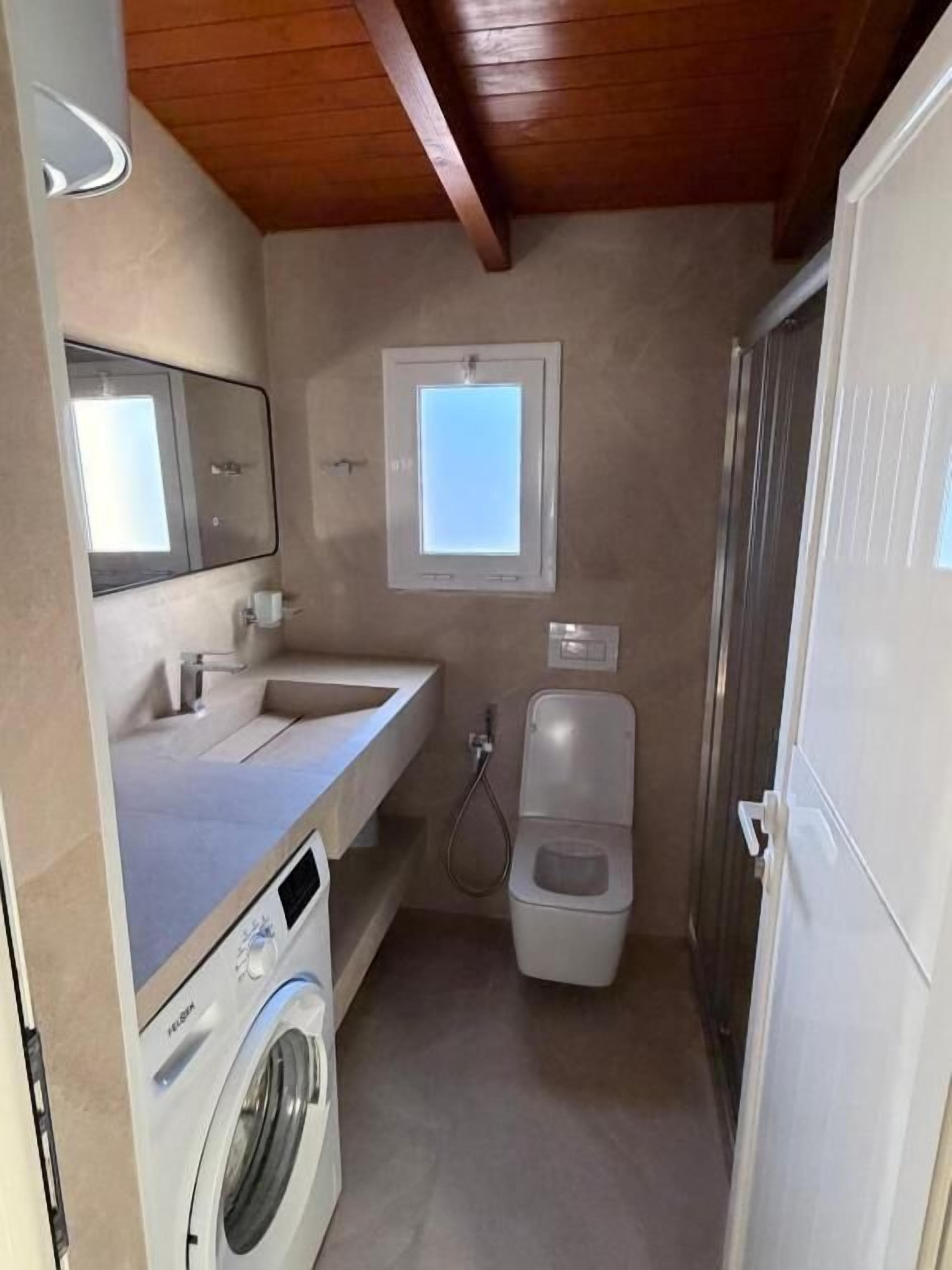 Un baño pequeño con lavadora, inodoro, lavamanos y ventana.