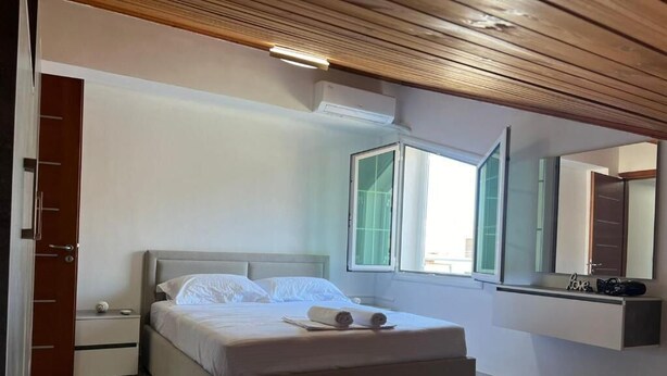 Un dormitorio con cama, mesita de noche, espejo y ventana.