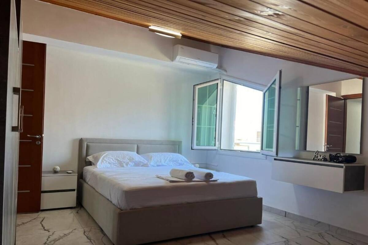 Un dormitorio con cama, mesita de noche, espejo y ventana.