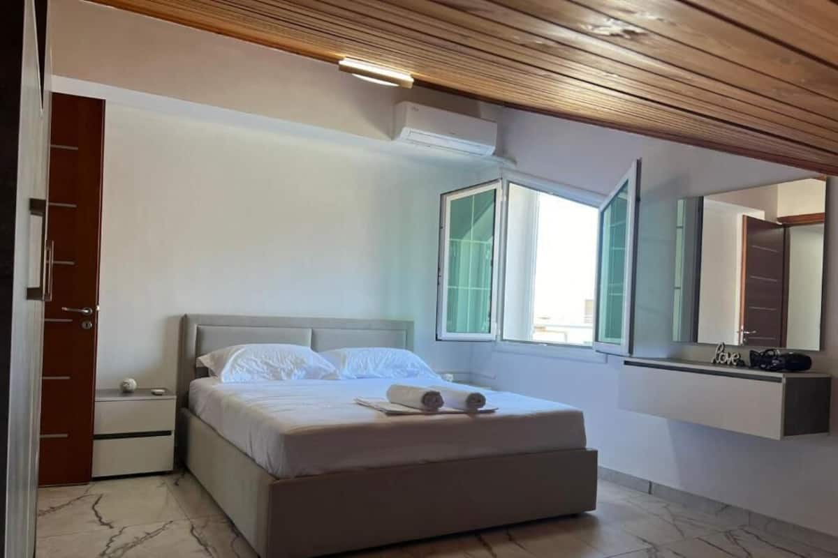 A bedroom with a bed, a nightstand, a mirror, and a window.