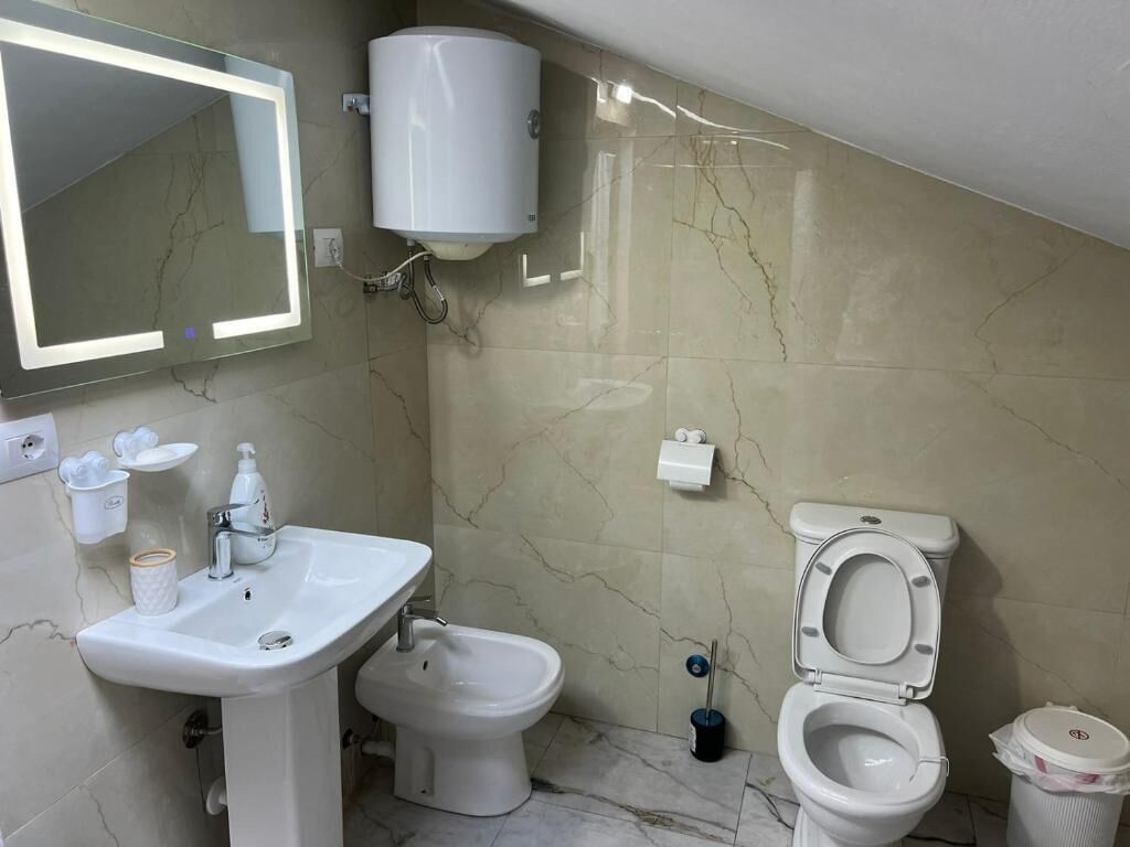 A bathroom with a sink, bidet, toilet, mirror, and a white toilet paper holder.