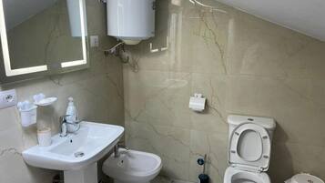A bathroom with a sink, bidet, toilet, mirror, and a white toilet paper holder.
