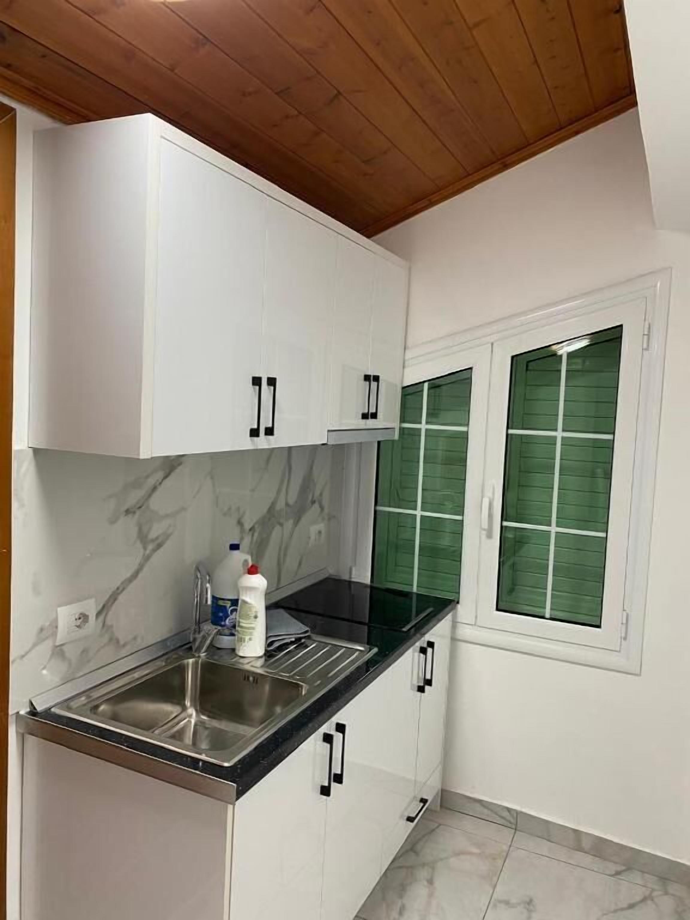 A kitchen with white cabinets, a black countertop, a stainless steel sink, and a window with green shutters.